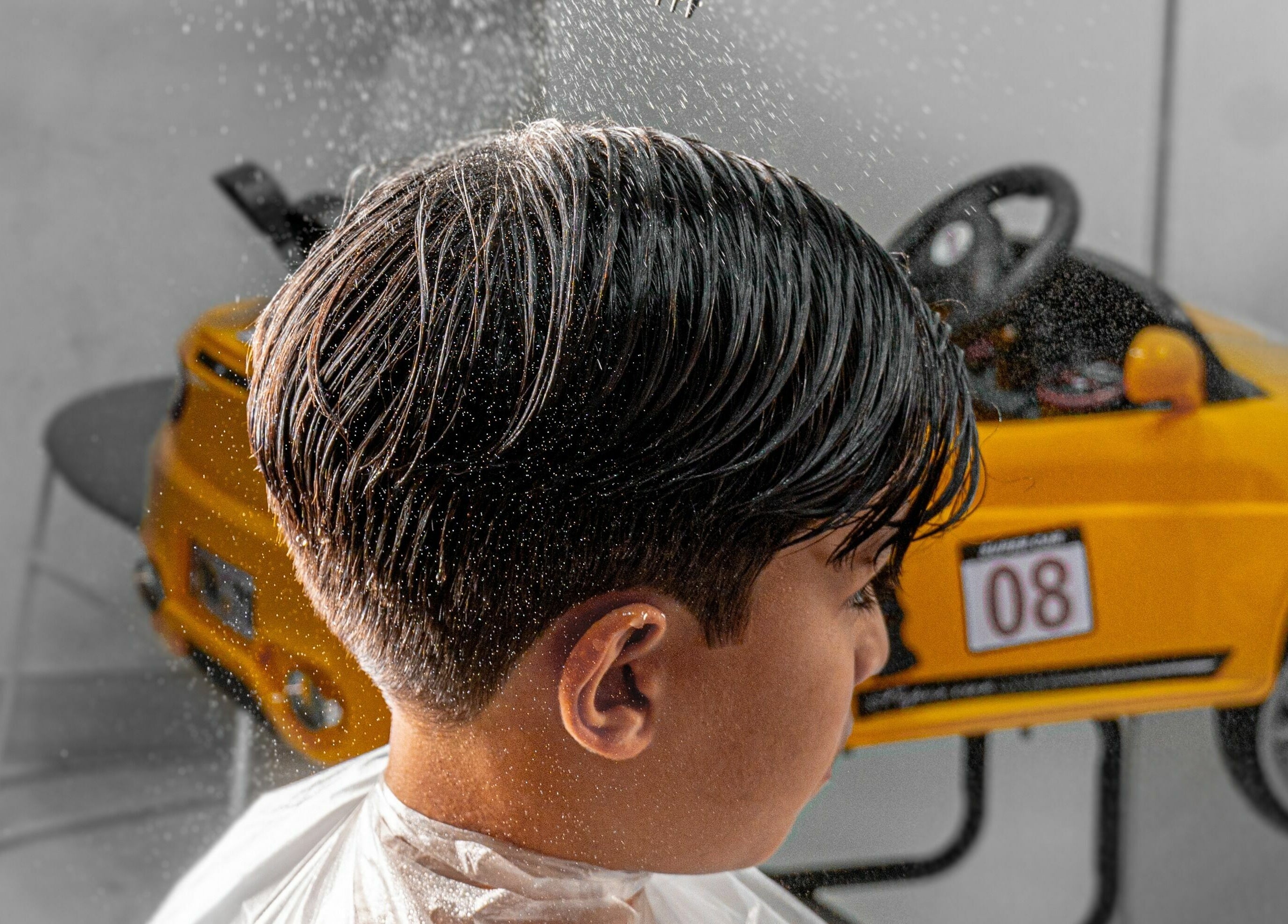Child receiving haircut at Katakeet Kids Saloon, Dubai, Dubai, AE, with water spray near a toy car.