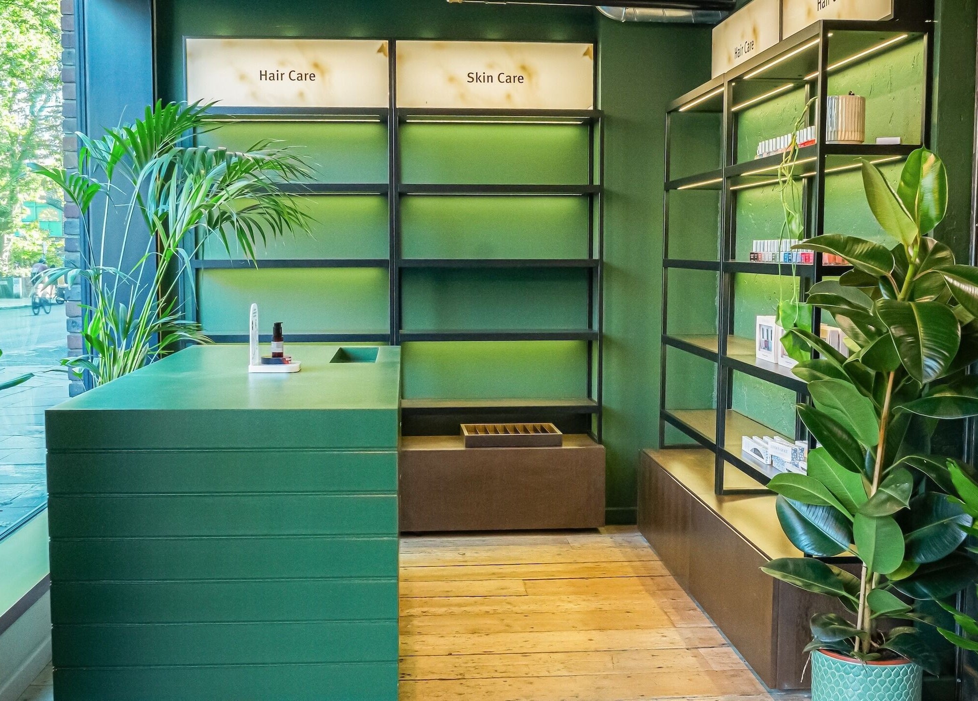 Modern green interior of Chop Chop London Camden, London, England, GB showcasing plants and skincare shelves.