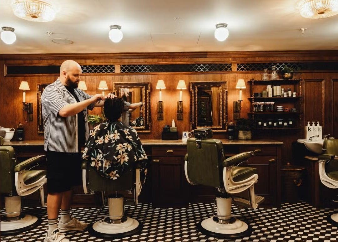 A barber styling hair at lite in London, England, GB, featuring vintage decor with wooden mirrors and retro chairs.