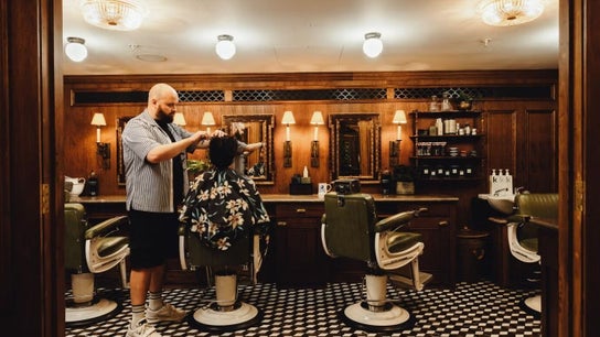 A barber styling hair at lite in London, England, GB, featuring vintage decor with wooden mirrors and retro chairs.