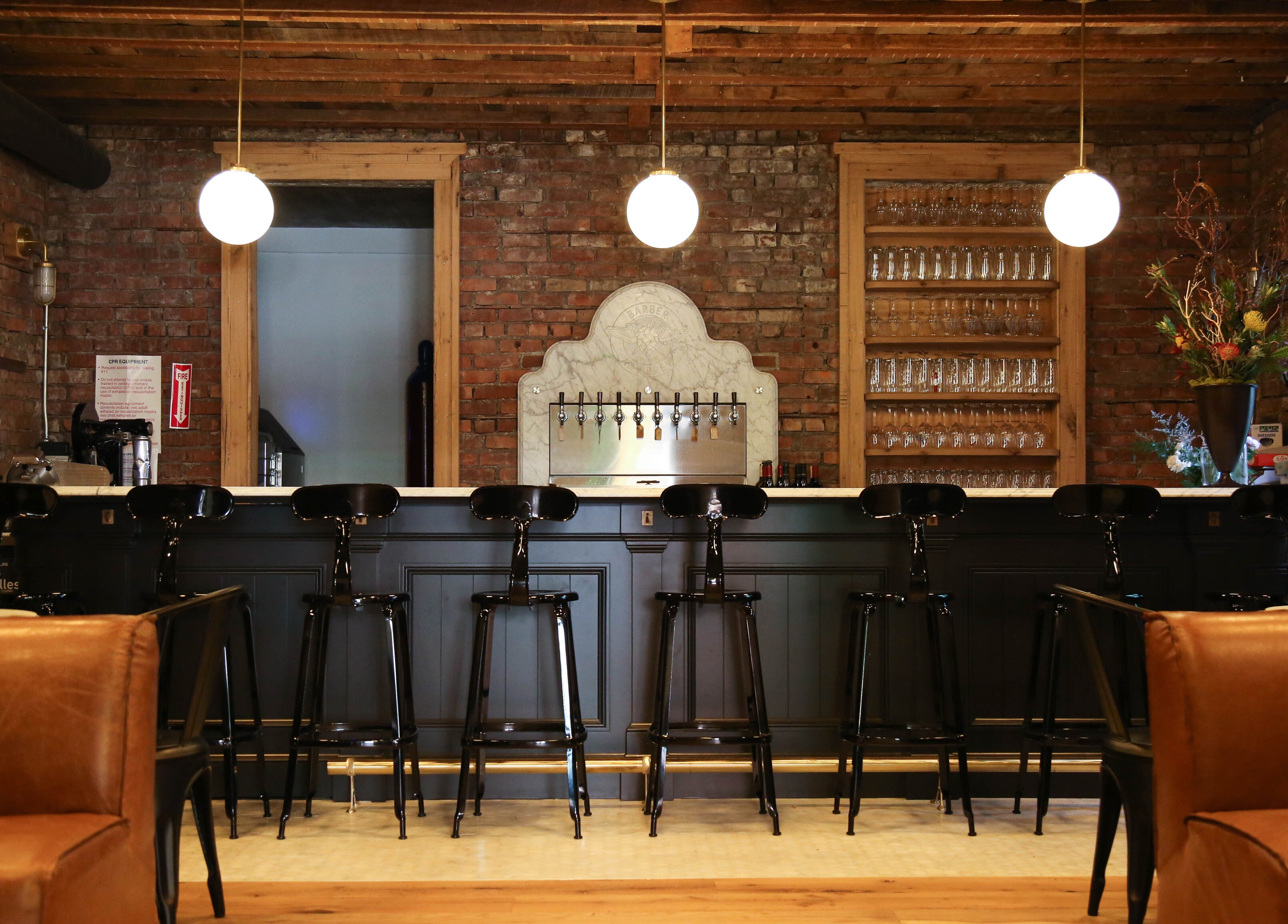 Inviting bar interior at Bar•Ber in Cold Spring, New York, US with a rustic brick backdrop and modern chairs.