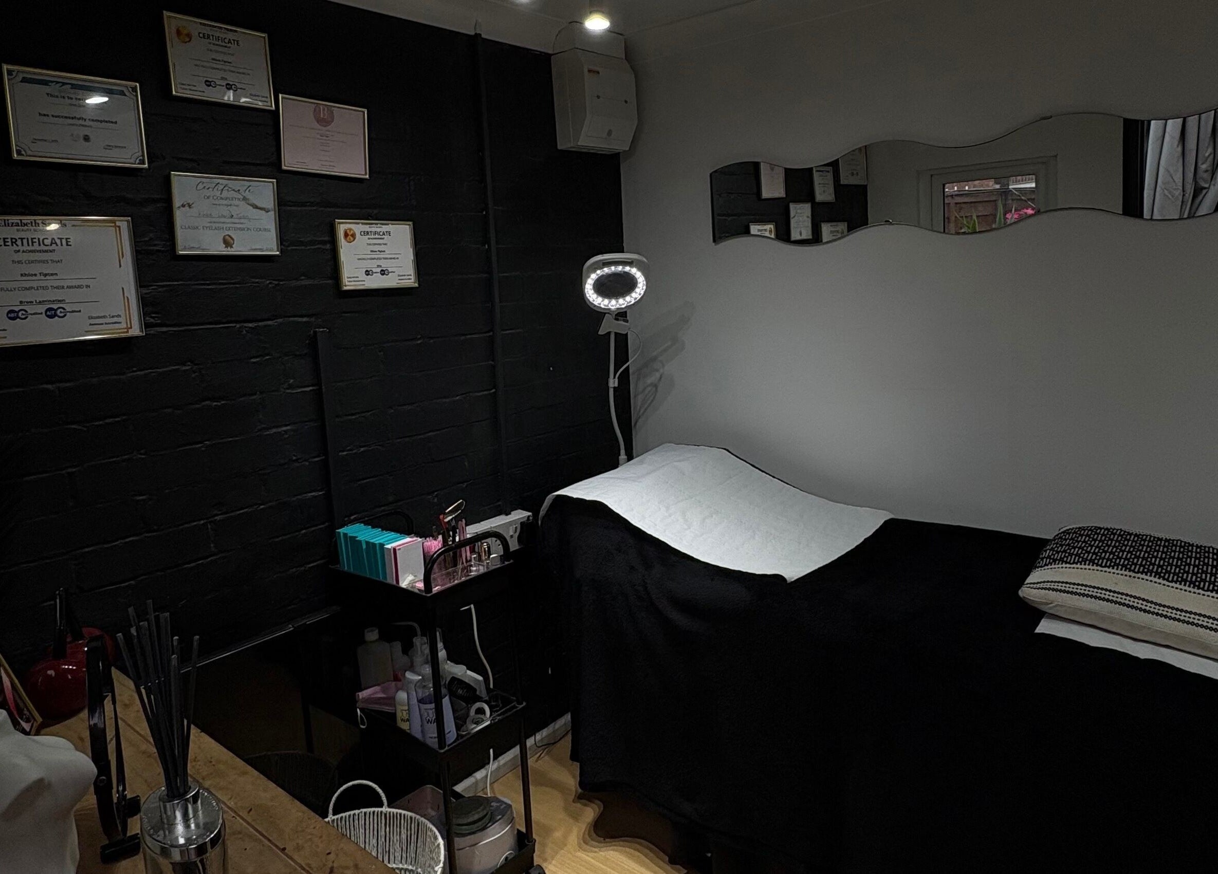 A serene treatment room at Builder and Brows by Khloe, Sandy, England, GB, showcasing certificates and a therapy bed.