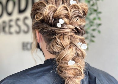 Intricate braided hairstyle with floral accents by Megan Gribbon Hair in Torquay, England, GB.