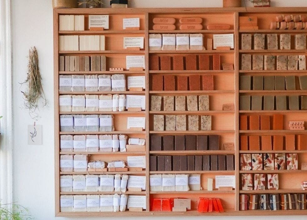 Diverse handmade soaps at Harvest Skincare, Birmingham, England, GB displayed neatly on wooden shelves.