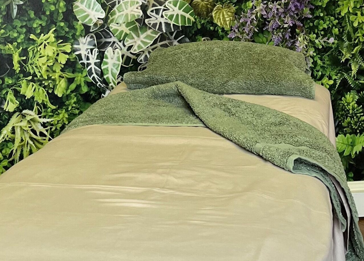 Calming green massage bed at Fern Bodyworks in Hextable, England, GB surrounded by lush foliage decor.