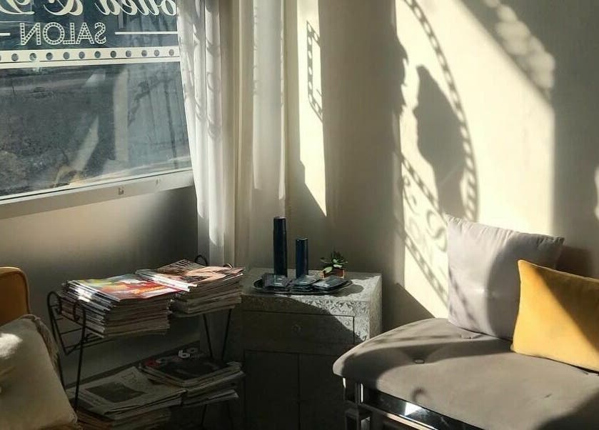 Bright sunlit lounge area at Dolled and Dapper Salon in San Francisco, California, US with cushions and magazines.