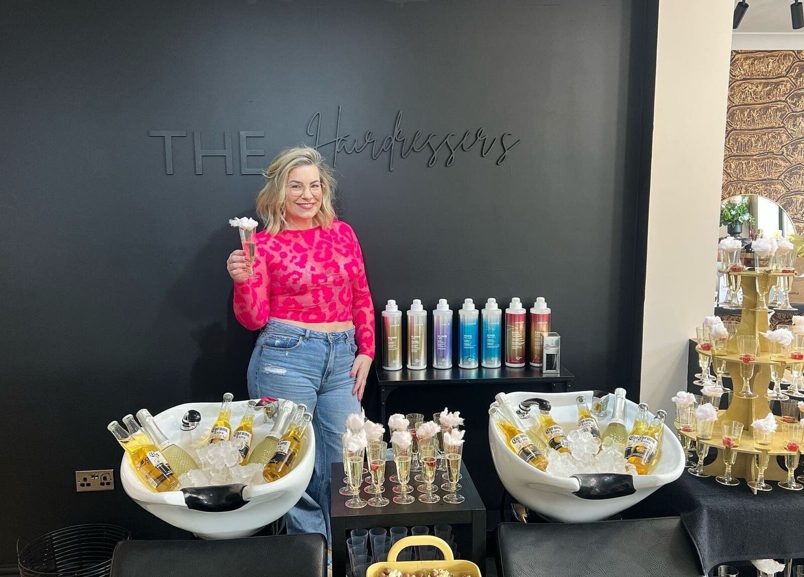 Person smiling in stylish salon THE Hairdressers, Lowestoft, England, GB with drinks and colorful products.