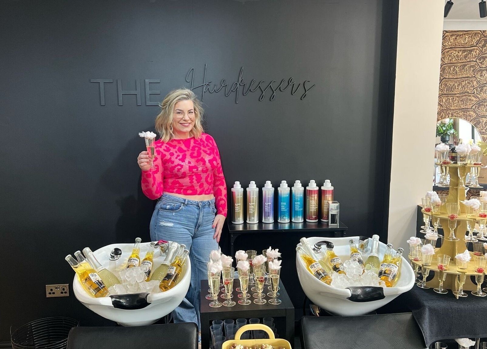 Person smiling in stylish salon THE Hairdressers, Lowestoft, England, GB with drinks and colorful products.