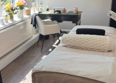 Cozy treatment room at The Beautique, Atherstone, England, GB with massage table and vibrant window flowers.