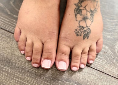 Tattooed foot with pale pink pedicure at The Beautique, Atherstone, England, GB on wooden floor.