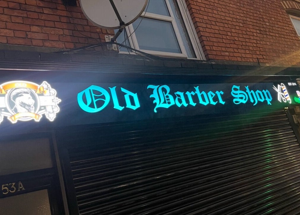 Illuminated sign of Old Barber Shop in Northampton, England, GB, showcasing vibrant neon lighting.