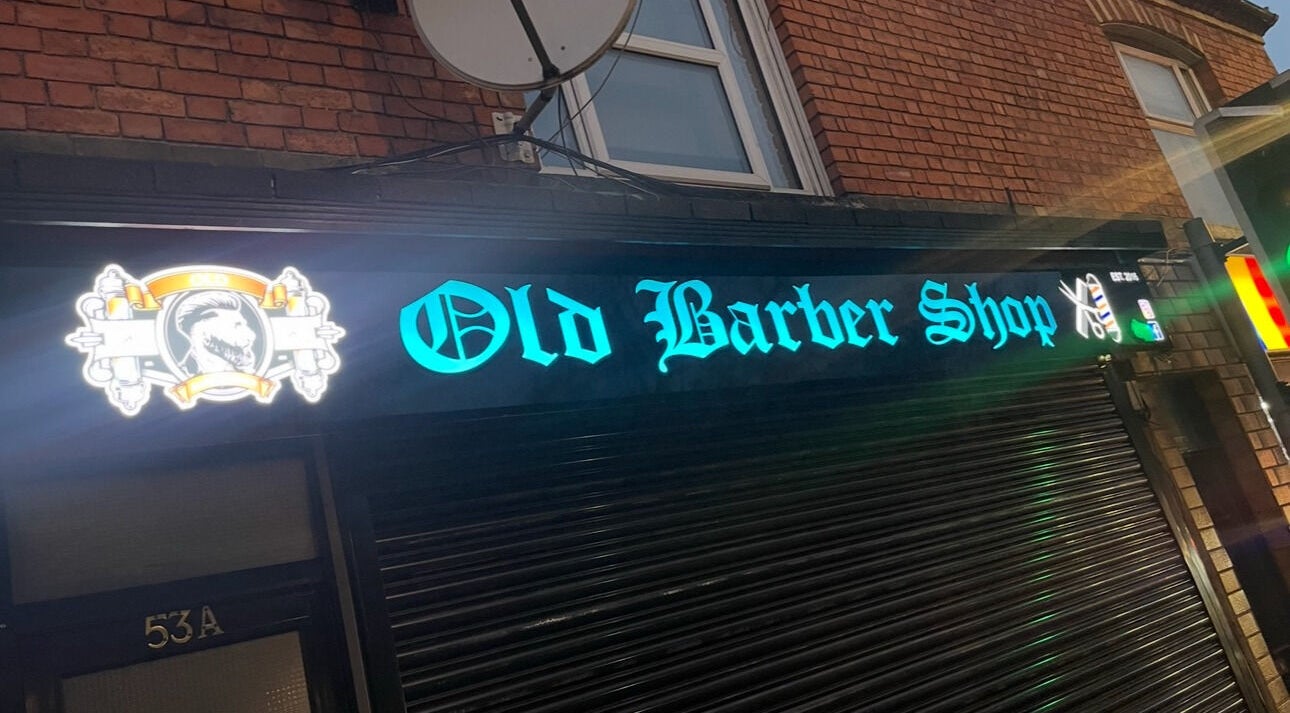 Illuminated sign of Old Barber Shop in Northampton, England, GB, showcasing vibrant neon lighting.