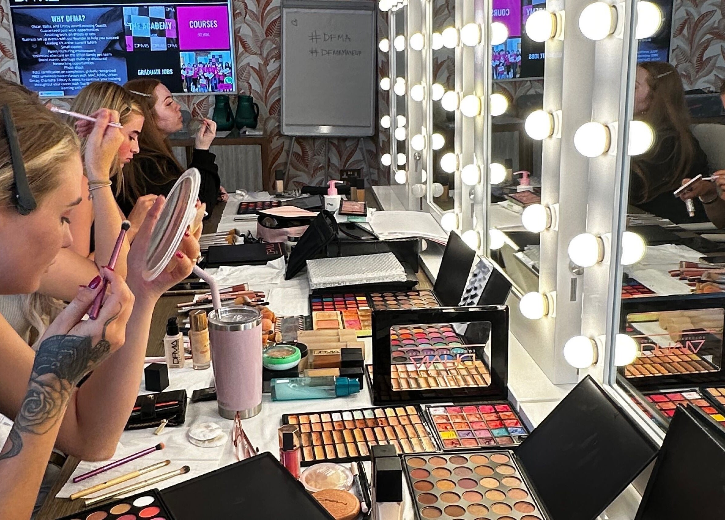 Students practicing makeup techniques at Dfma Make Up & Hair Bar in Poole, England, GB with palettes and brushes.