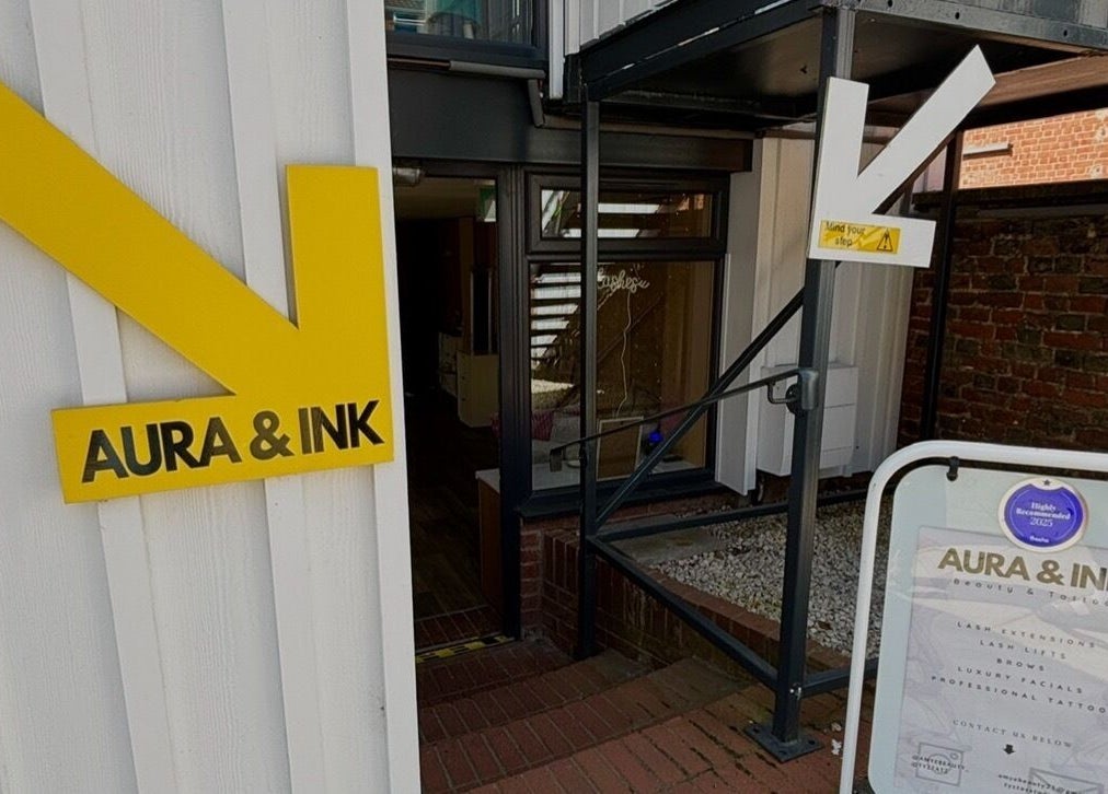 Entrance of Aura & Ink near AmyEBeauty in Sudbury, England, GB, featuring a modern yellow sign.