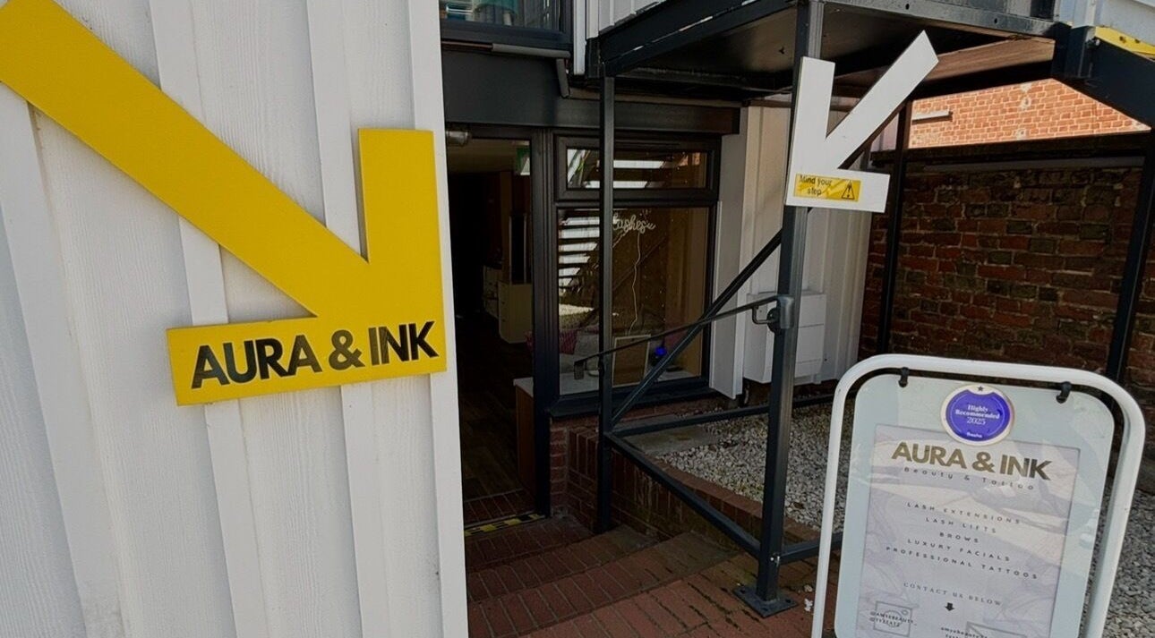 Entrance of Aura & Ink near AmyEBeauty in Sudbury, England, GB, featuring a modern yellow sign.