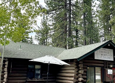 Emerald Grove Salon, a rustic log cabin, nestled in South Lake Tahoe, California, US, surrounded by tall trees.
