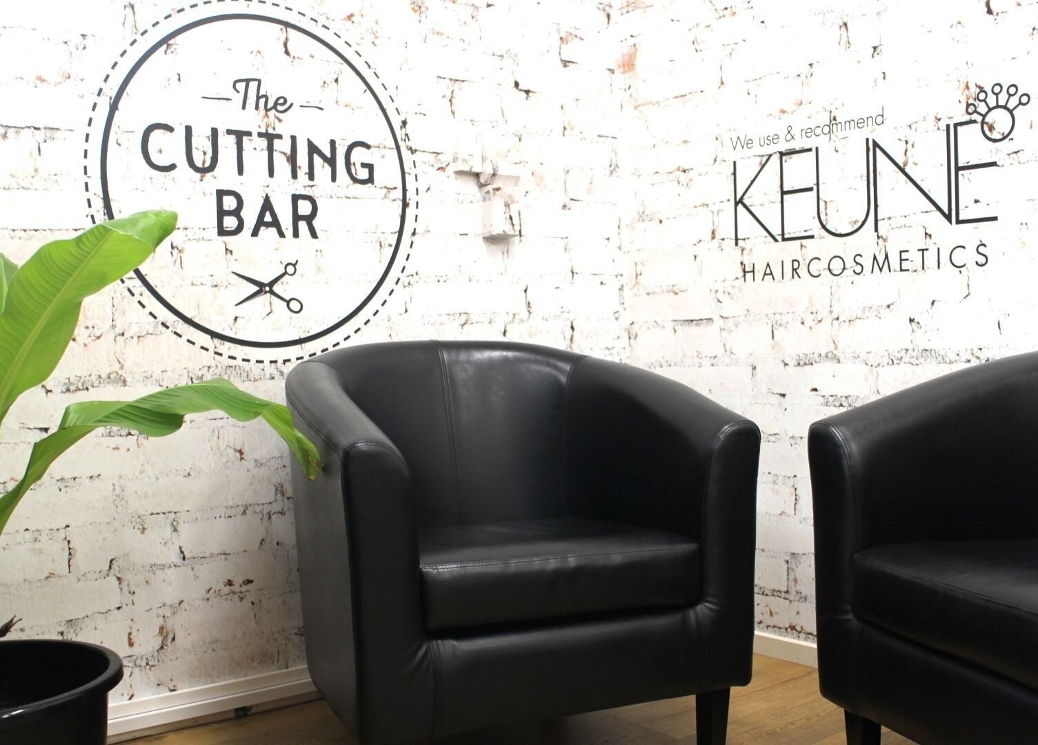 Stylish seating at The Cutting Bar, Nelson, NZ with black chairs and plant against a modern white brick wall.