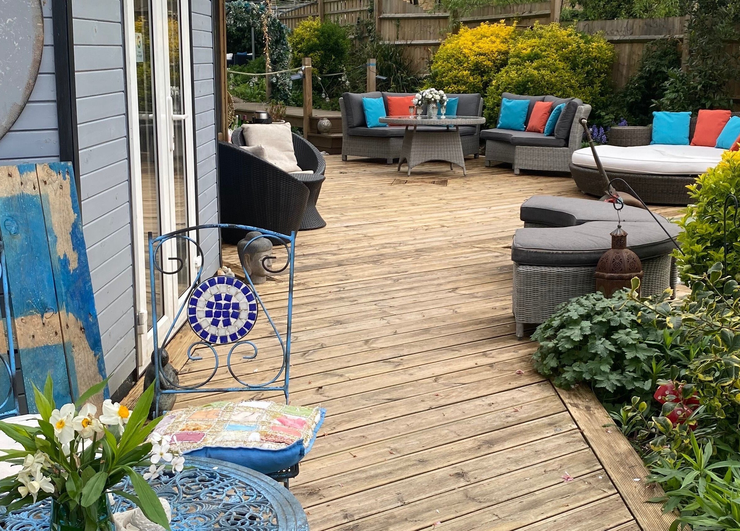 Charming patio seating at Touching Lives, Hampton, England, GB, surrounded by lush greenery and vibrant cushions.