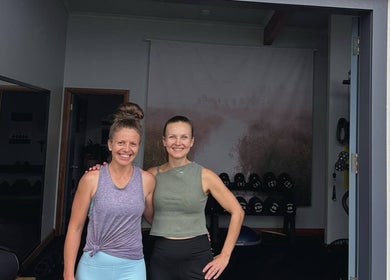 Two women smiling at Studio You, Burnt Pine, NF, standing near gym equipment.