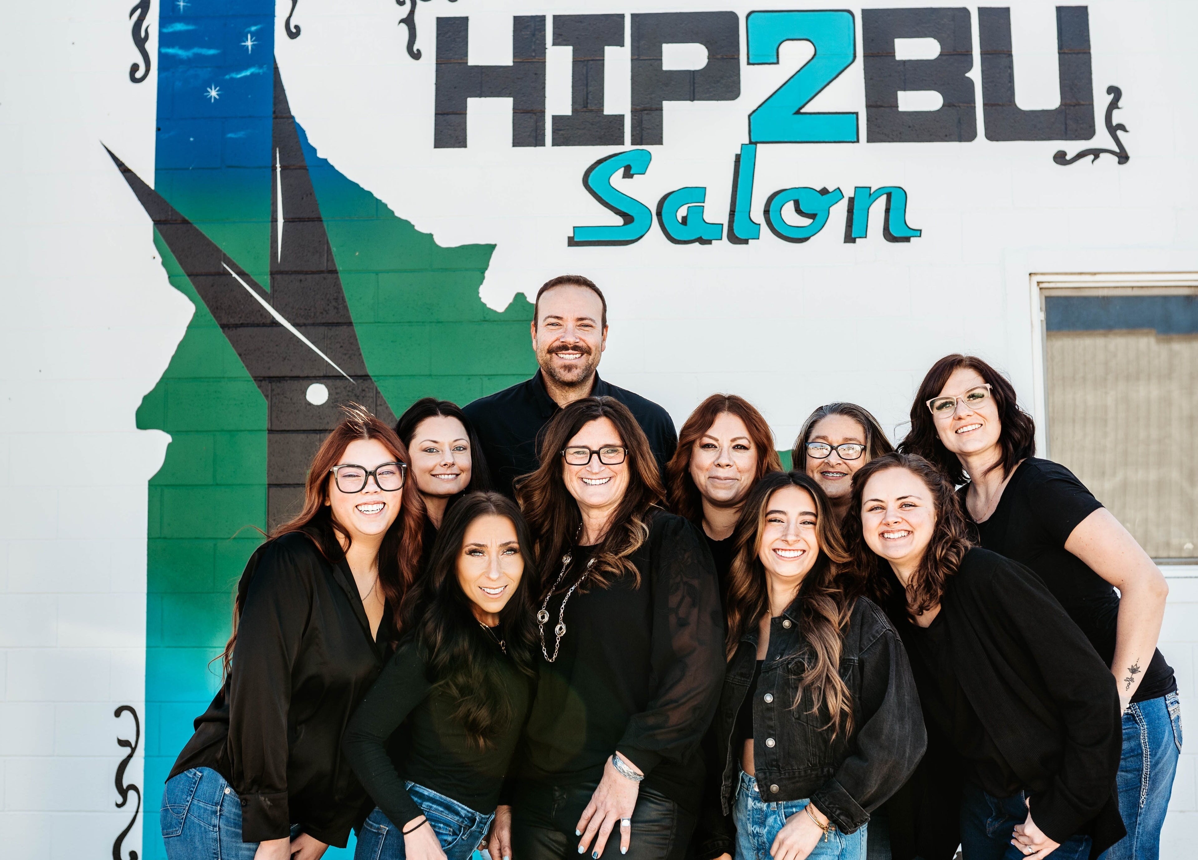 Friendly team at Hip2BU Salon, Kimberly, Idaho, US, smiling in front of vibrant wall mural.