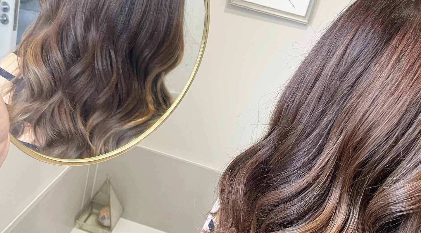 Elegant wavy hairstyle at Laura Waterworth Hair, Dunmurry, Northern Ireland, GB, reflected in circular mirror.