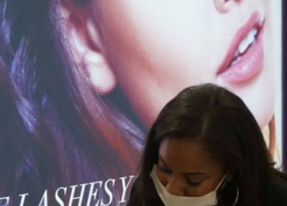 Aesthetician working at Lashes by Shareen in Kettering, England, GB, with a backdrop of a beauty model poster.