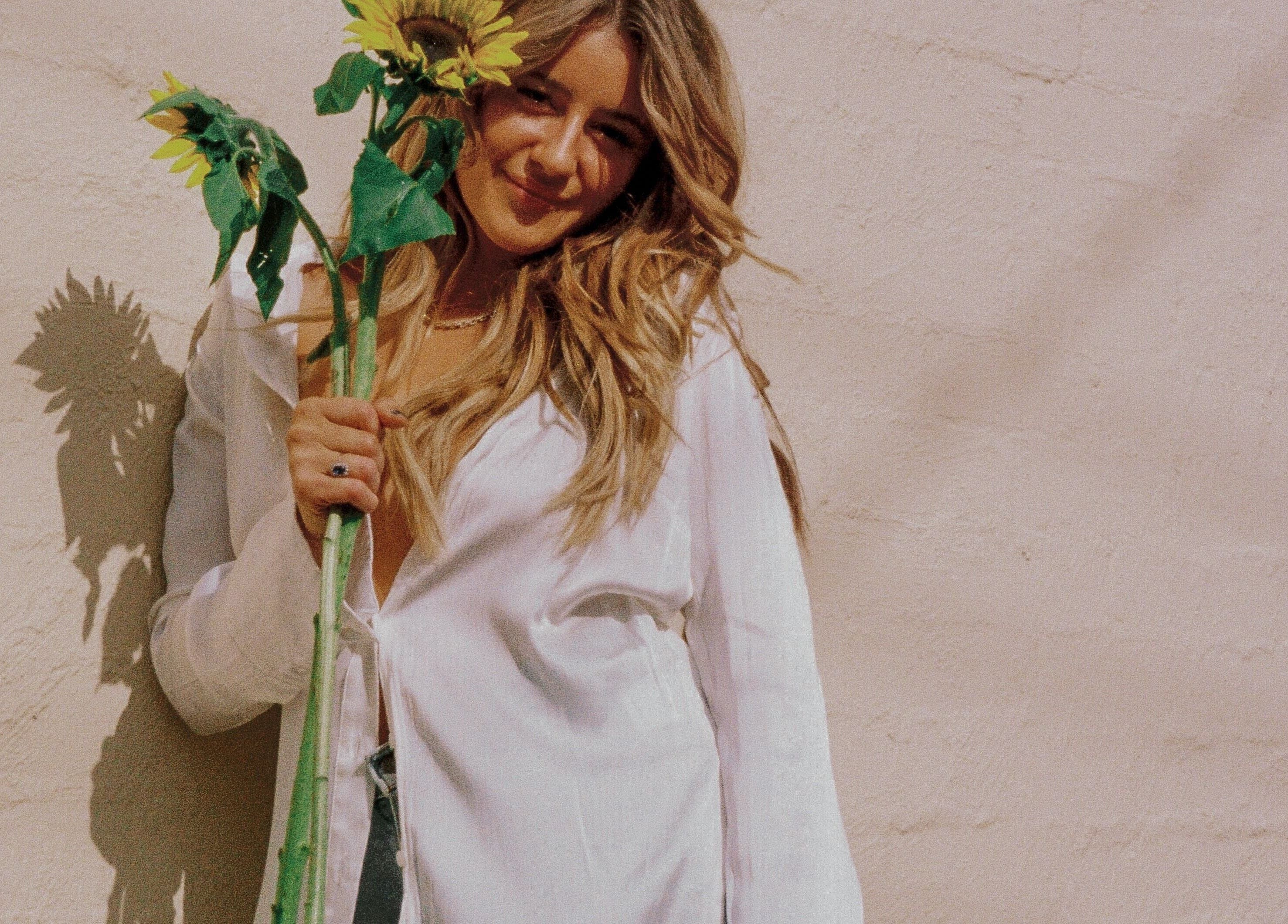 Woman smiling with sunflower, highlighting Addie Robins Hair's natural charm in Melbourne, Victoria, AU.