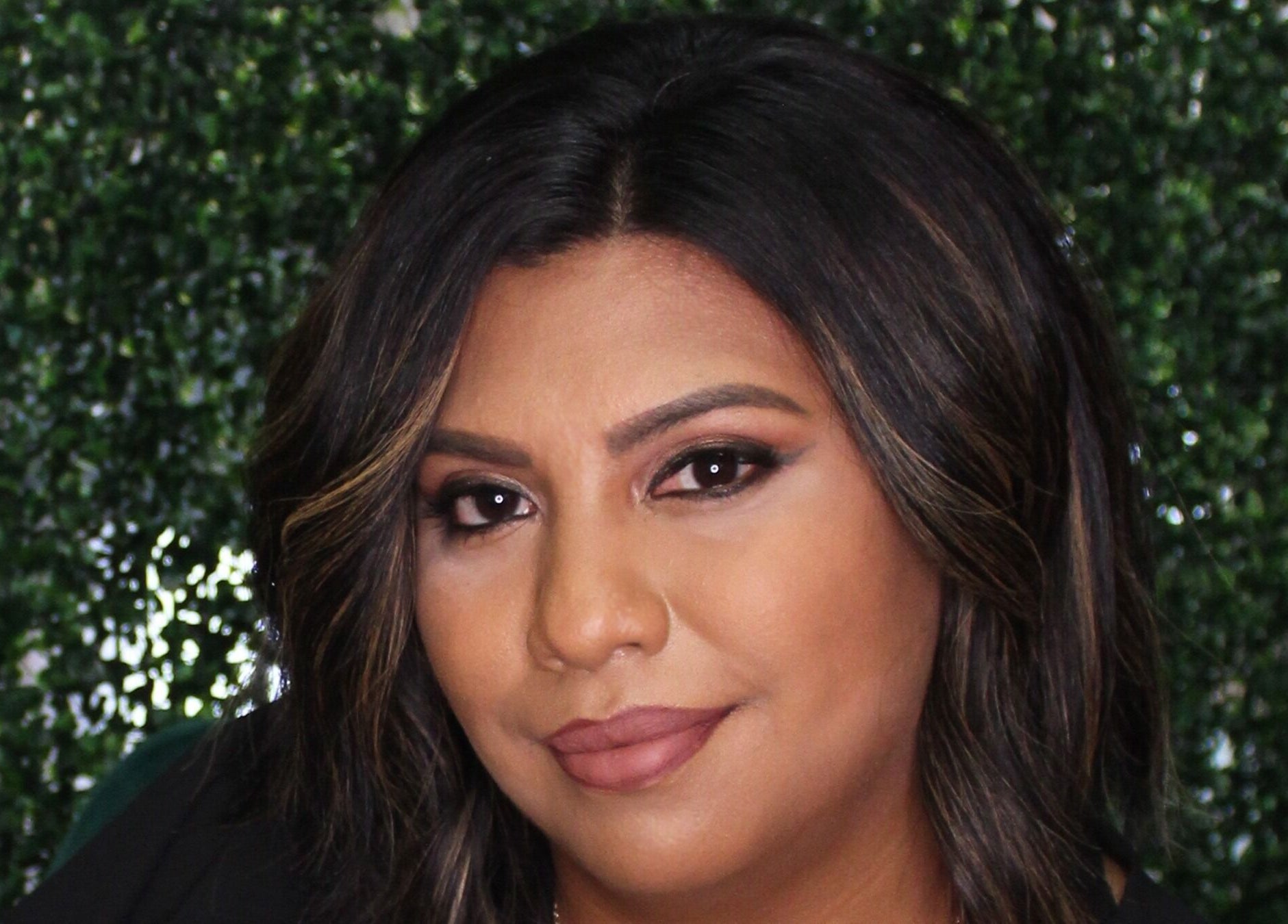 Client styled at Fringe Salon in Elkhart, Indiana, US with lush hair framing her face against a green backdrop.