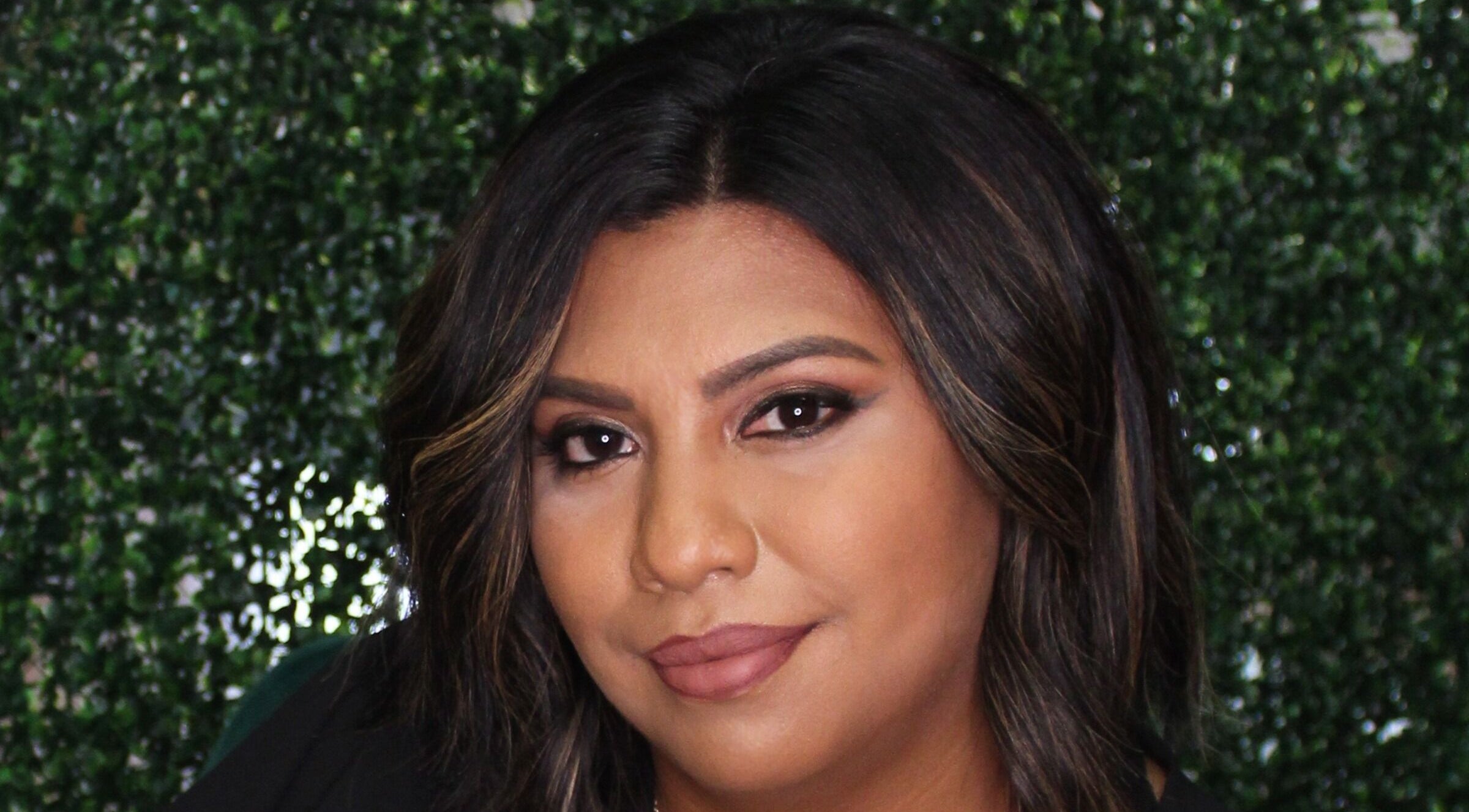 Client styled at Fringe Salon in Elkhart, Indiana, US with lush hair framing her face against a green backdrop.