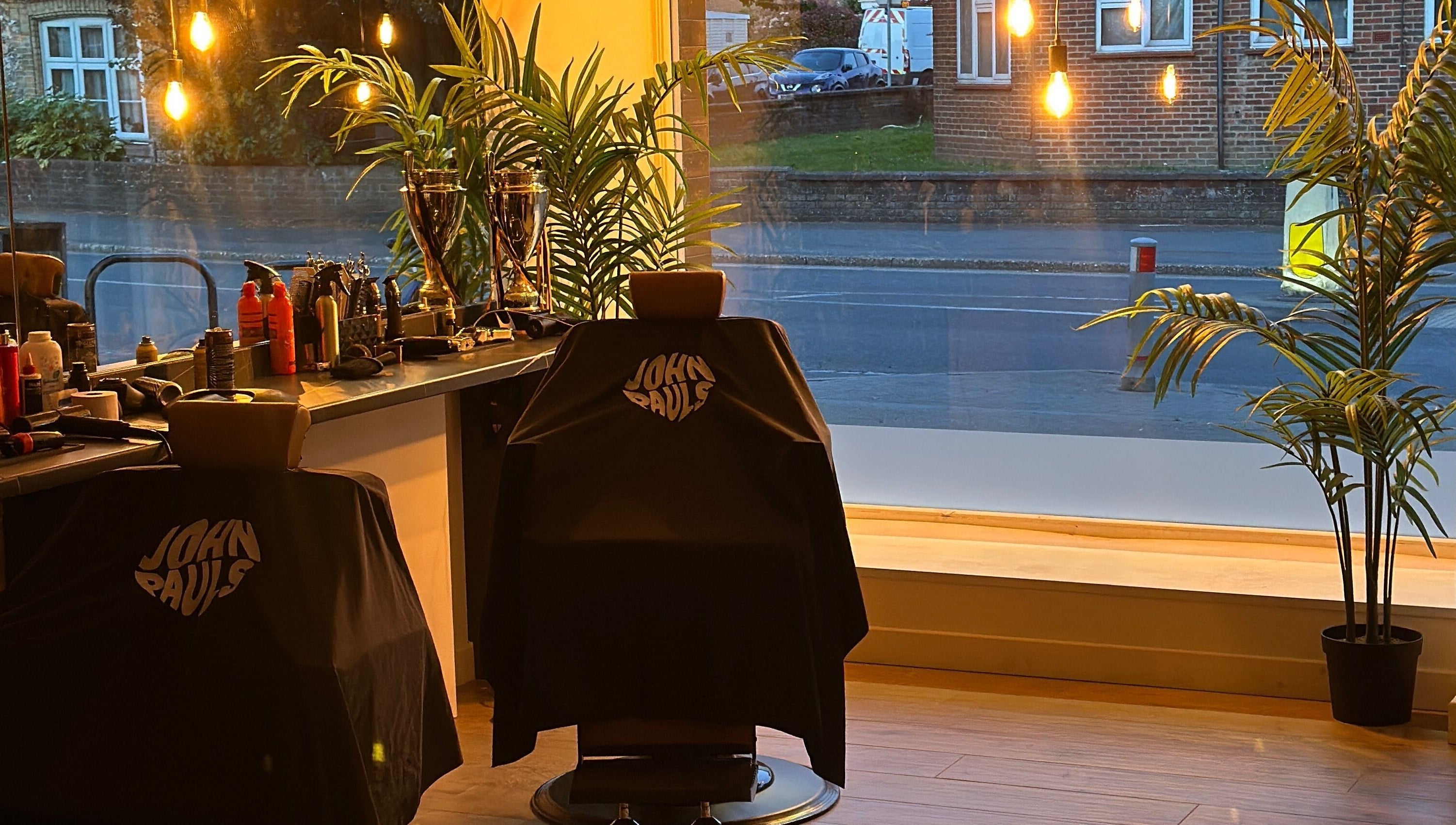 Interior of John Pauls Barbershop in Lancing, England, with stylish chairs and warm lighting.