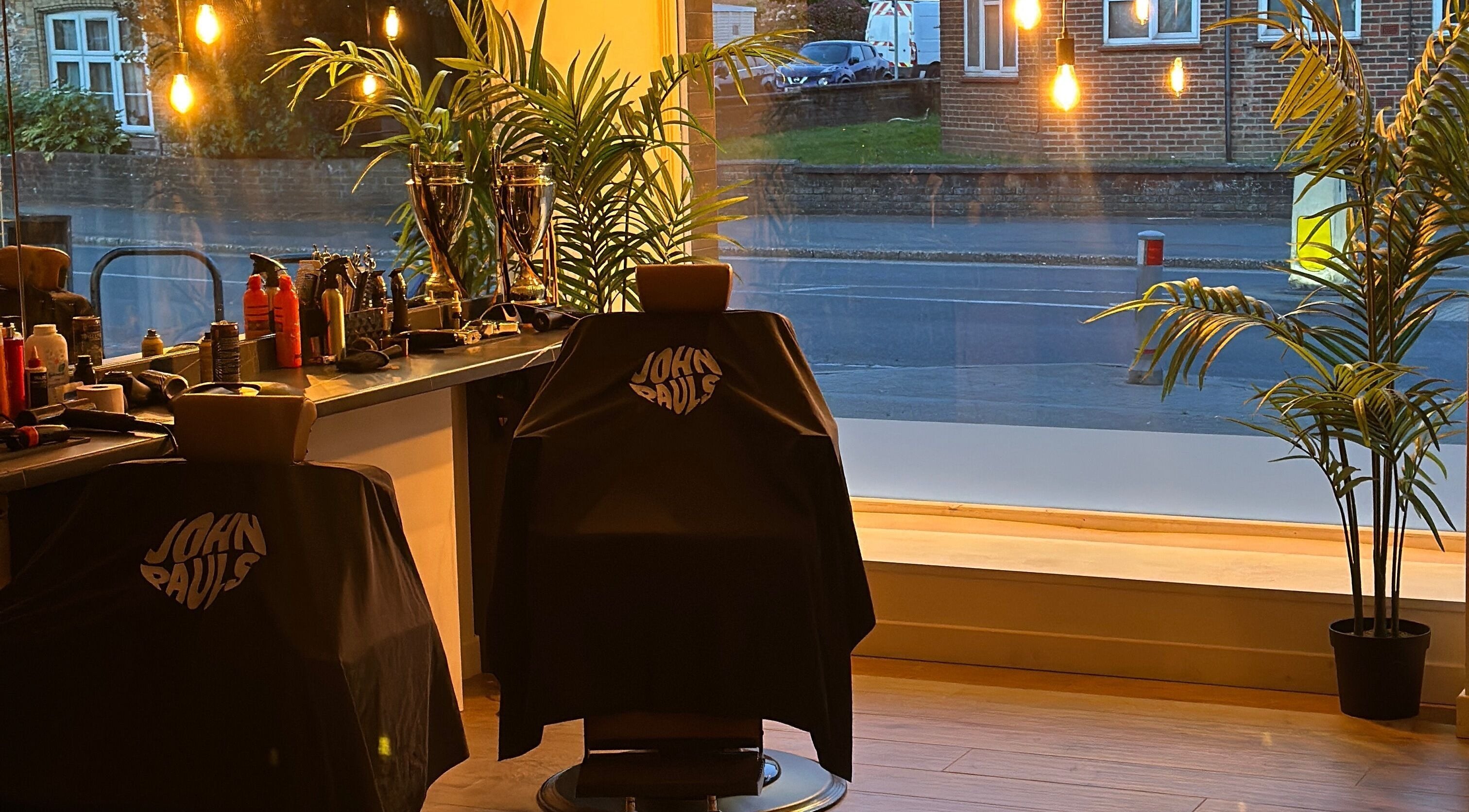 Interior of John Pauls Barbershop in Lancing, England, with stylish chairs and warm lighting.