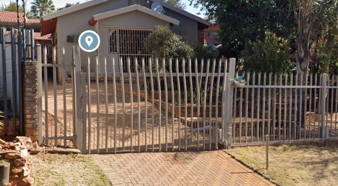 Gated entrance to The Nail Booth in Krugersdorp, Gauteng, ZA surrounded by lush greenery.