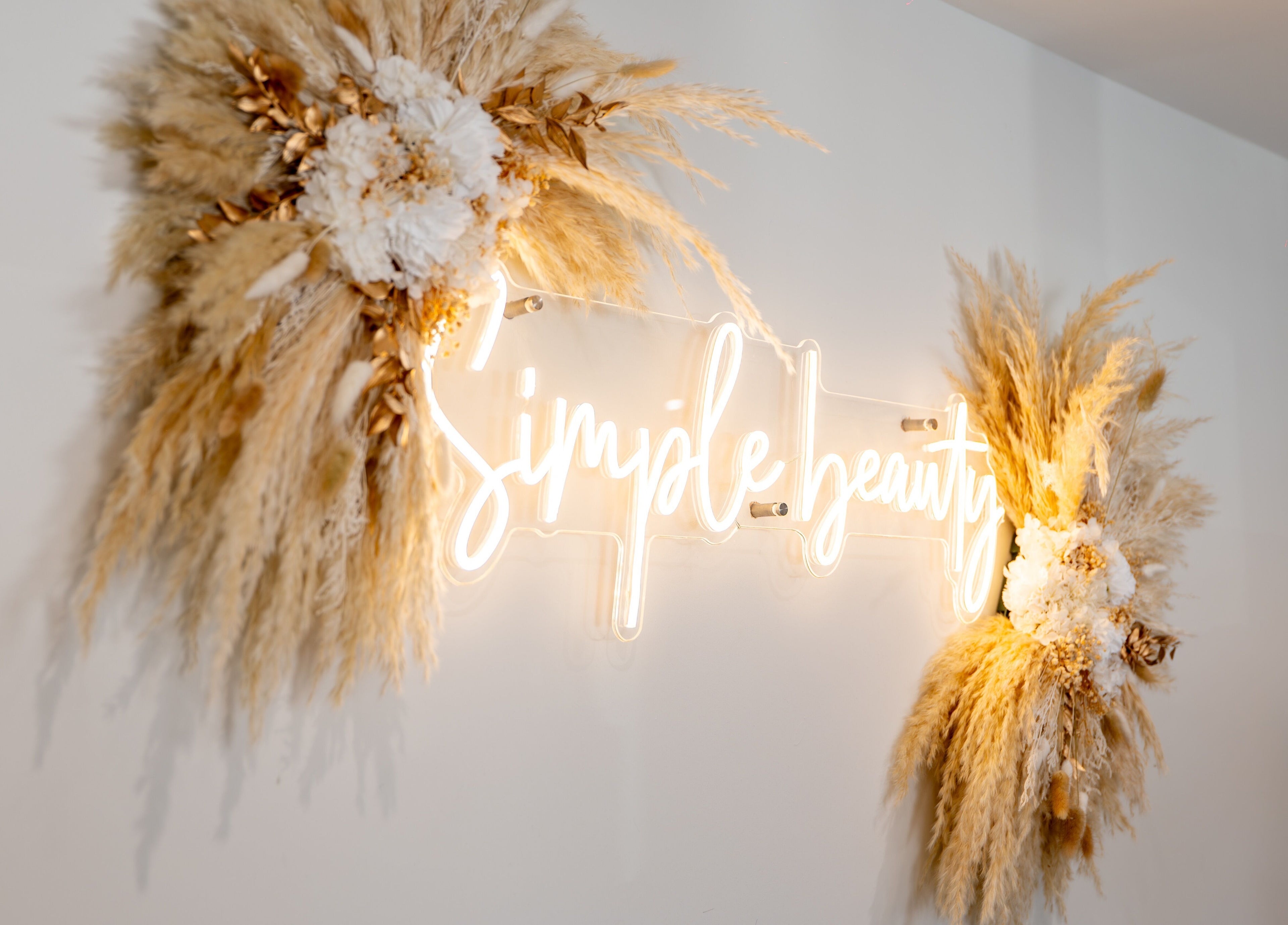 Elegant neon sign at Simple Beauty, Cullompton, England, GB, framed by lush dried florals.