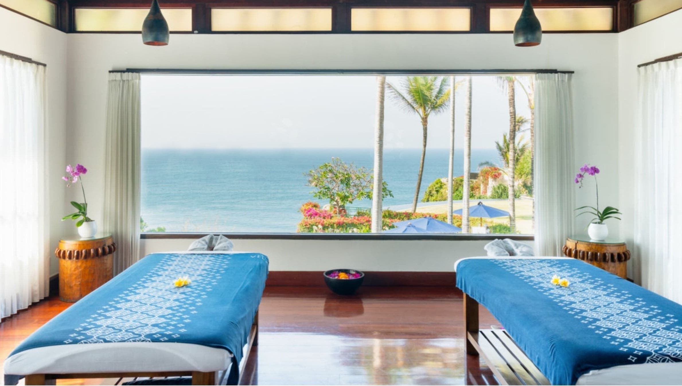 Peaceful Vela Spa room in Bali, Bali, ID with ocean view, blue massage tables, and orchids.