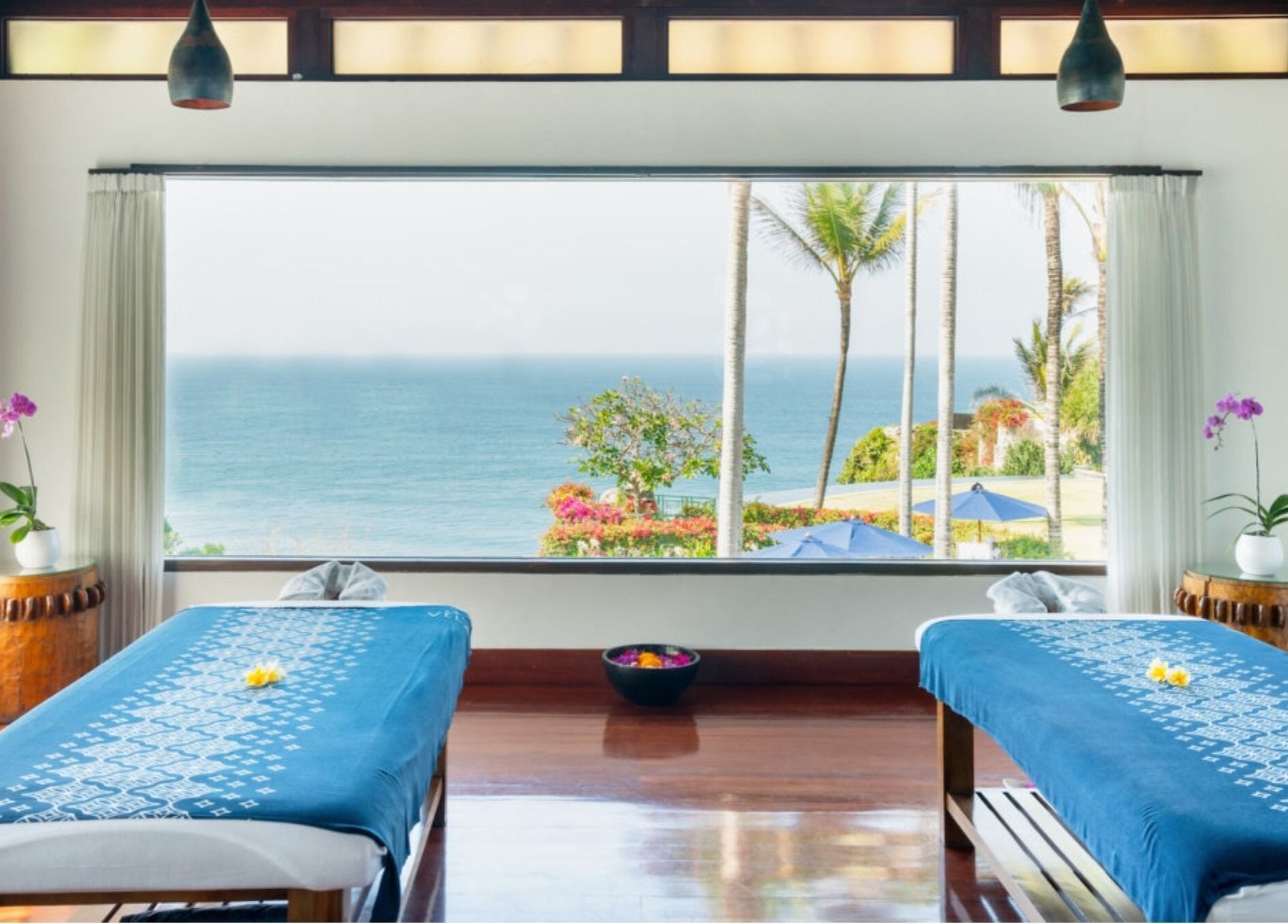 Peaceful Vela Spa room in Bali, Bali, ID with ocean view, blue massage tables, and orchids.
