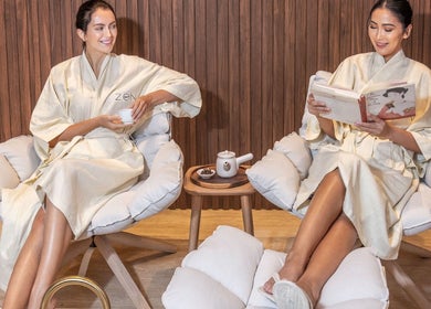 Two women relaxing in robes at Zen Spa, Doha, Doha, QA, enjoying tea and reading in comfort.