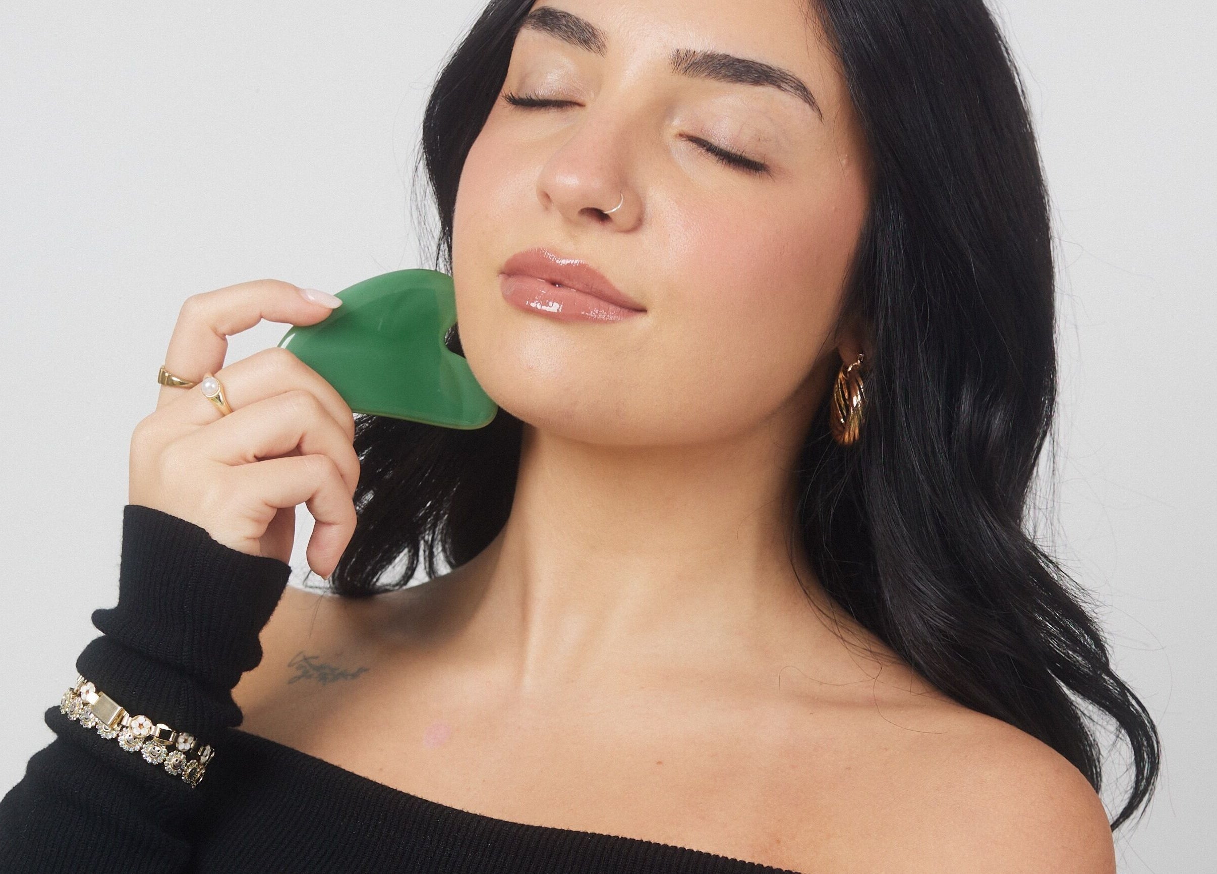 Woman using gua sha tool on cheek at Lashesxbeautybar, Vaughan, Ontario, CA for enhanced skin glow.