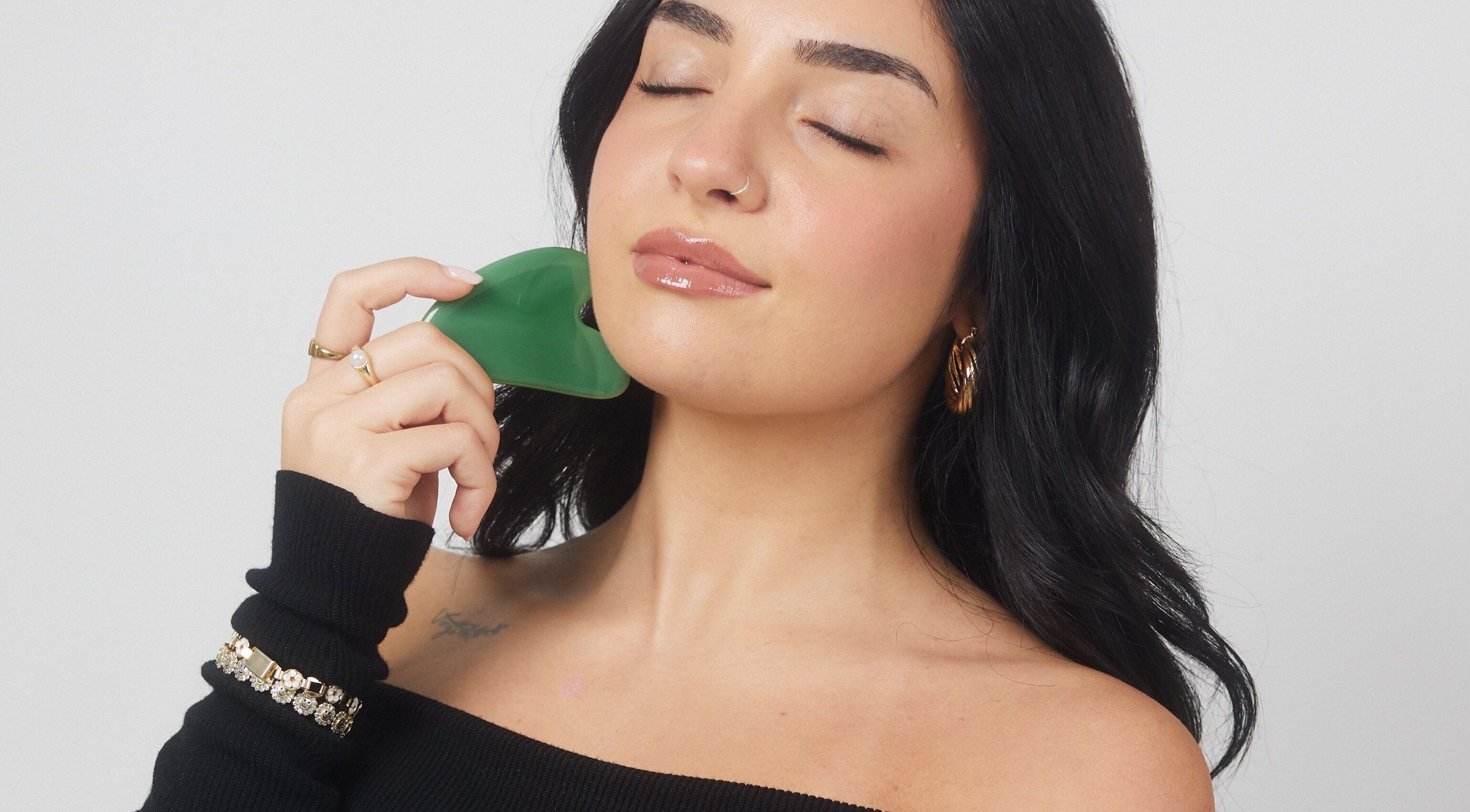 Woman using gua sha tool on cheek at Lashesxbeautybar, Vaughan, Ontario, CA for enhanced skin glow.