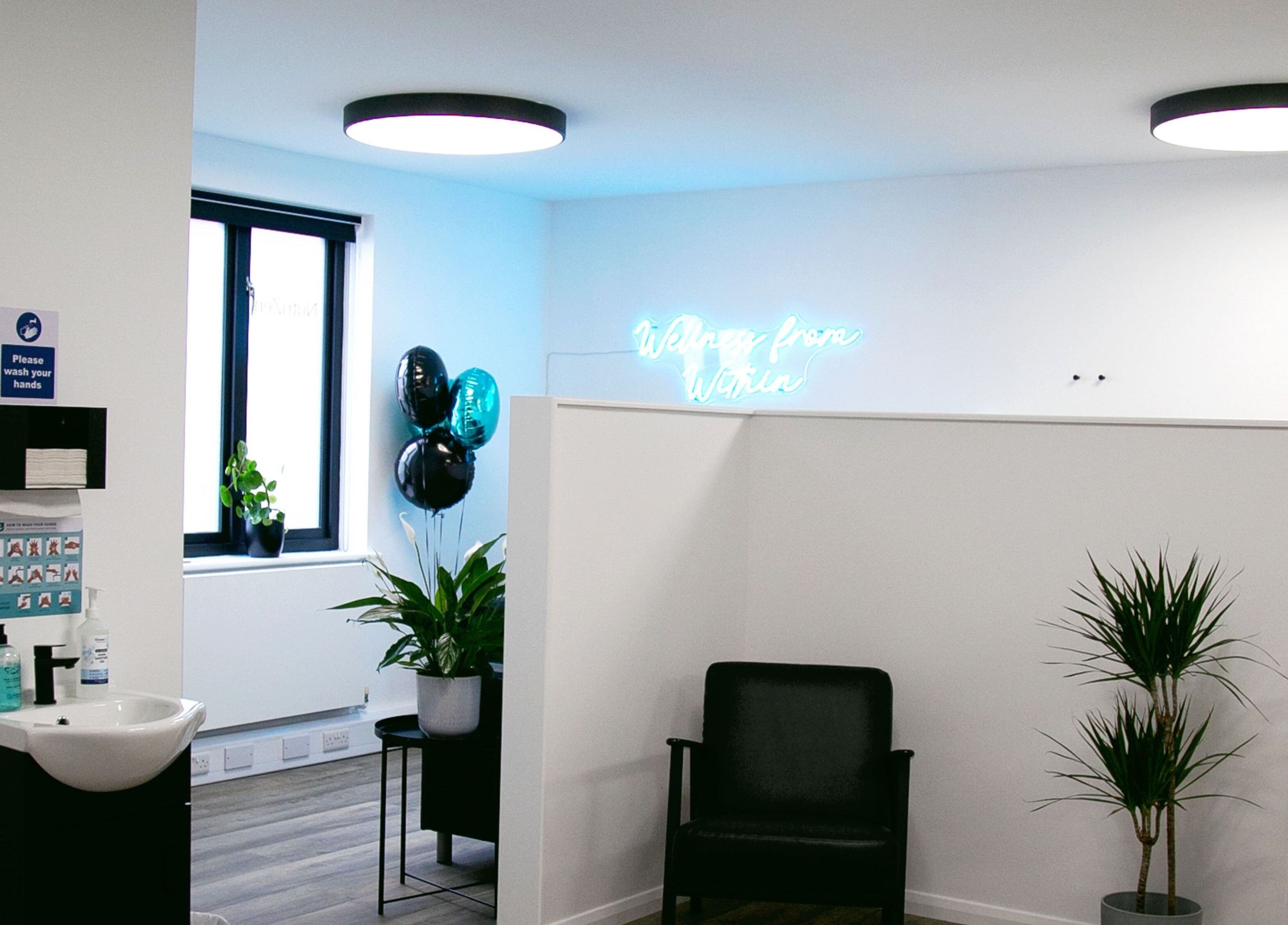 Modern serene lobby at NutriZen Wellness Centre, Wolverton, England, GB. Features plants, seating, and neon sign.