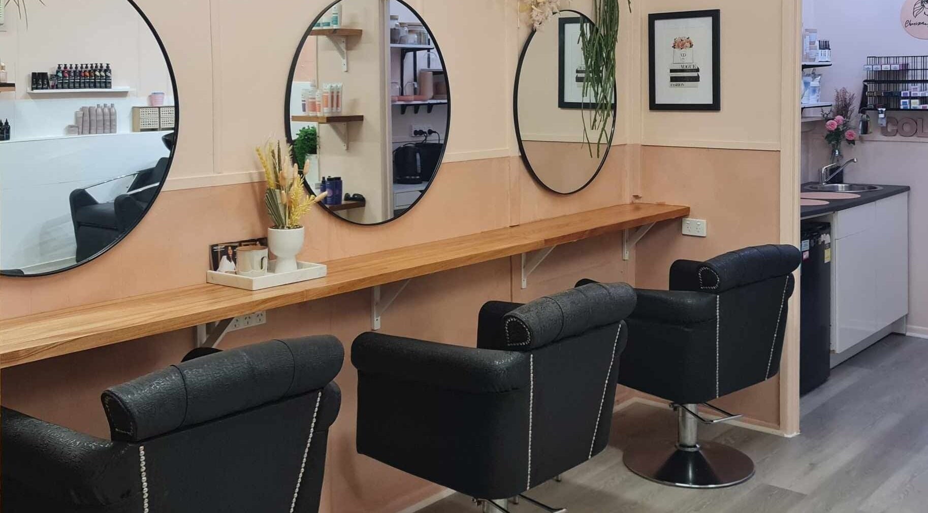Chic styling station at Charizma Hair Design in Bald Hills, Queensland, AU, showcasing sleek black chairs and round mirrors.