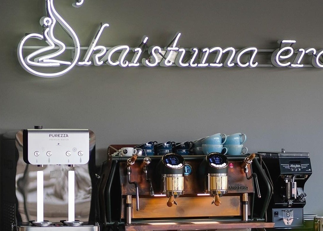 Skaistuma ēra Jelgava features a stylish coffee nook with neon signage above espresso machines.