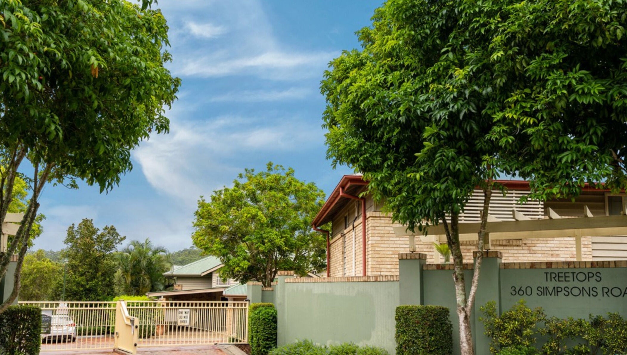 Entrance of Curly & Blonde, Bardon, Queensland, AU, surrounded by lush greenery and clear blue sky.
