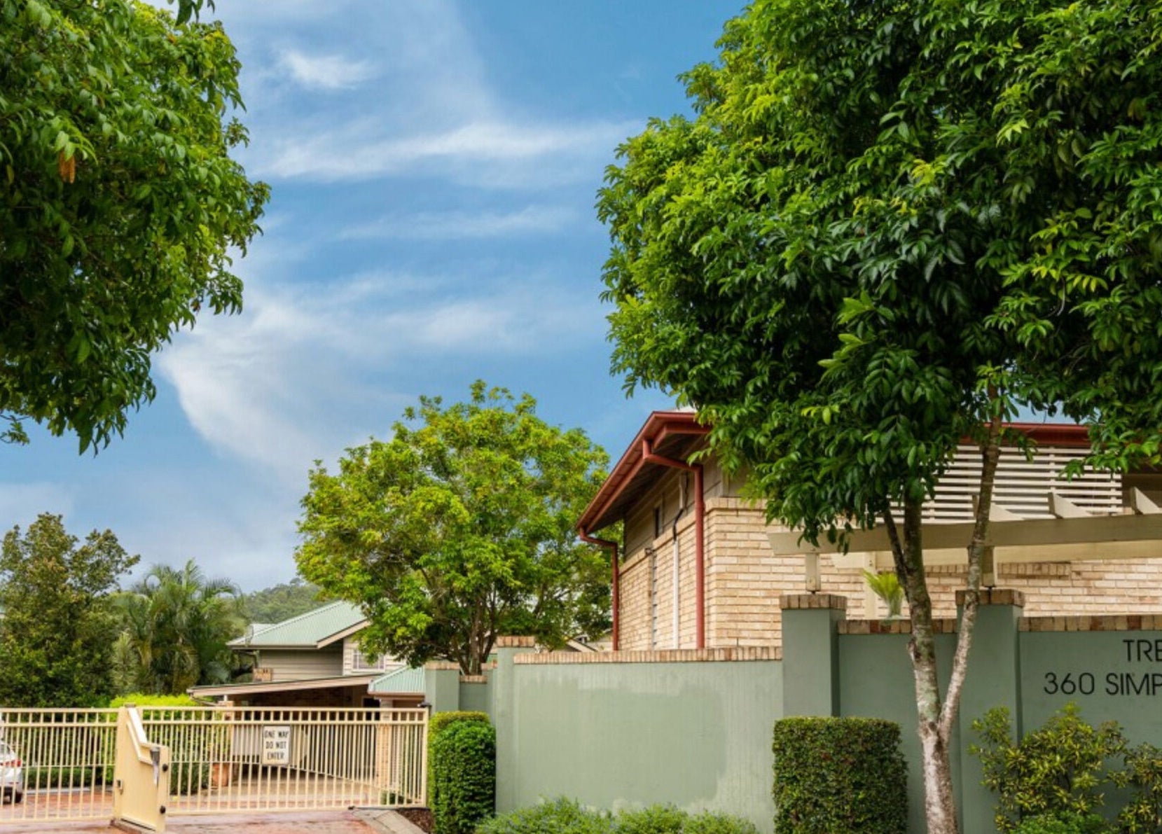 Entrance of Curly & Blonde, Bardon, Queensland, AU, surrounded by lush greenery and clear blue sky.