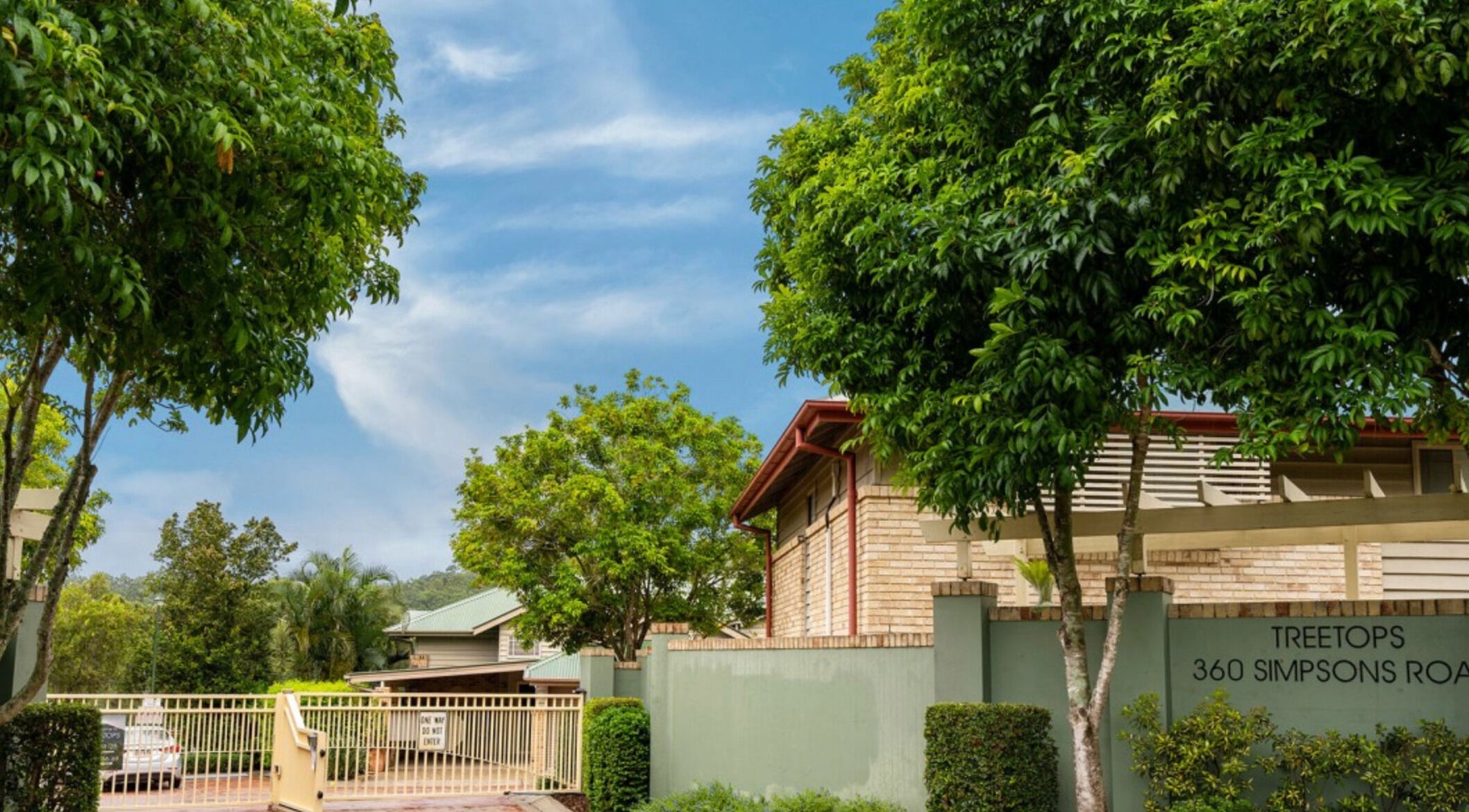 Entrance of Curly & Blonde, Bardon, Queensland, AU, surrounded by lush greenery and clear blue sky.