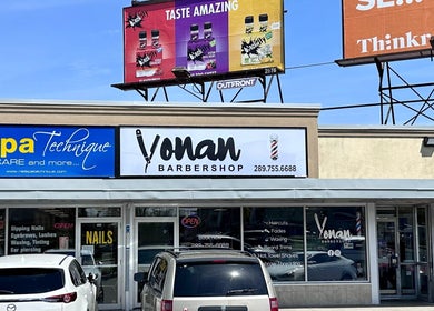 Exterior of Yonan's Barber Shop in Hamilton, Ontario, CA with vibrant signage and parked cars.