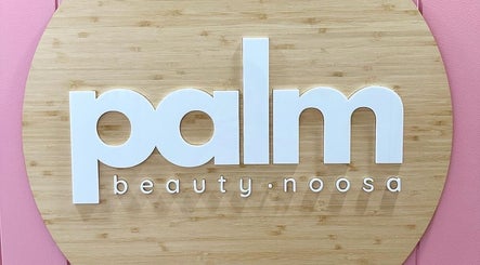 Elegant Palm Beauty Noosa wooden sign in Noosaville, Queensland, AU against a soft pink background.