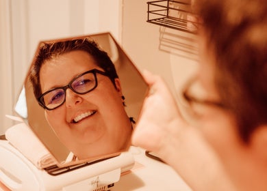 Vrolijke klant bij Zen&Zo in Hemiksem, BE kijkt tevreden in spiegel tijdens wellnessbehandeling.