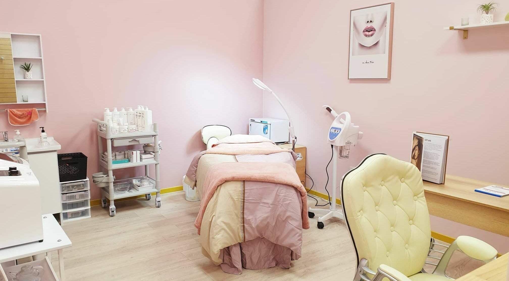Cozy spa room with pink walls at Hello Beautiful Lounge - Hastings, NZ, featuring a treatment bed and equipment.