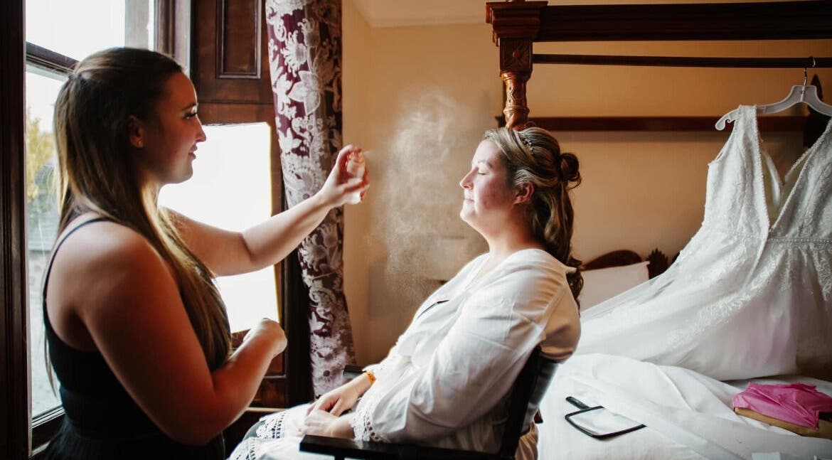 Makeup artist at CM Beauty, Blairgowrie, Scotland, GB spritzing bride near wedding gown.
