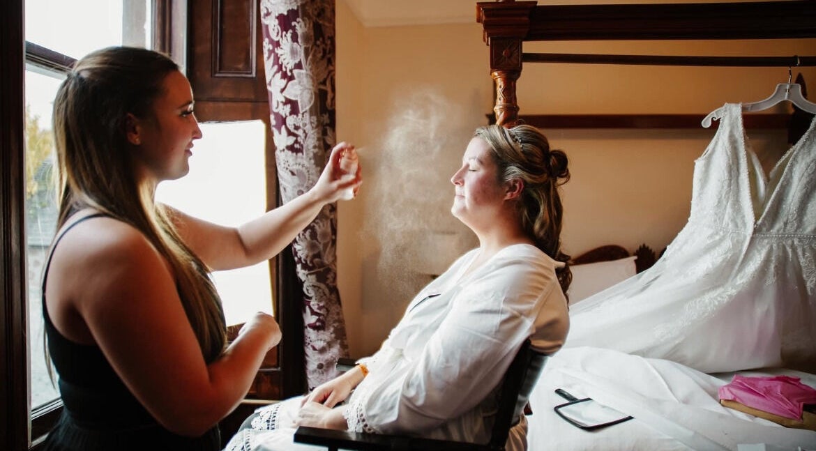 Makeup artist at CM Beauty, Blairgowrie, Scotland, GB spritzing bride near wedding gown.